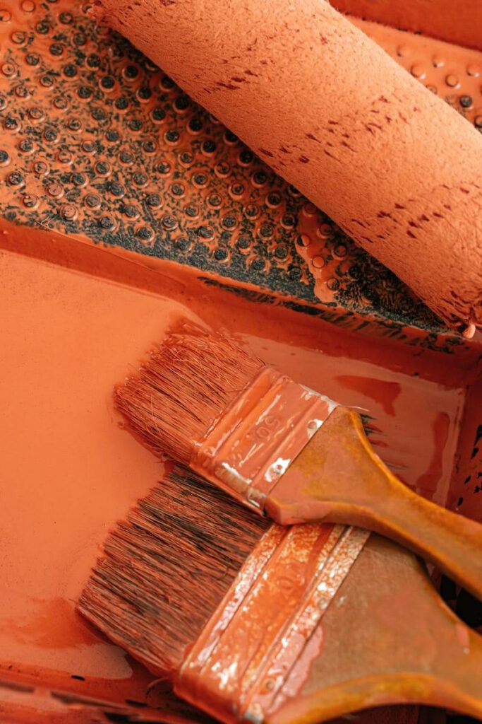 Two paintbrushes and a roller coated with orange paint in a tray, perfect for DIY projects.